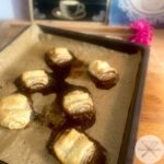 Frisch gebackene vegane Franzbrötchen auf Backblech mit pinker Dekoblume im Hintergrund